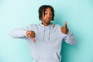 Genç Afro-Amerikalı adam mavi arka planda izole edilmiş, baş parmağını kaldırıyor, zor seçim konsepti