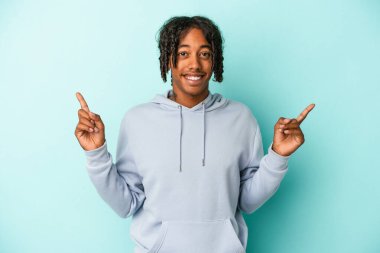 Mavi arka planda izole edilmiş genç Afrikalı Amerikalı iki parmağı da boş bir alan gösteriyor..