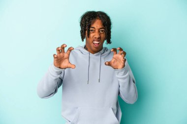 Genç Afrikalı Amerikalı adam mavi arka planda izole edilmiş pençelerini kedi taklidi yaparken gösteriyor, agresif bir hareket..