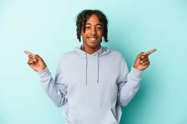 Genç Afro-Amerikan adam mavi arka planda izole edilmiş farklı kopya alanlarını işaret ederek, onlardan birini seçiyor, parmaklarıyla gösteriyor.