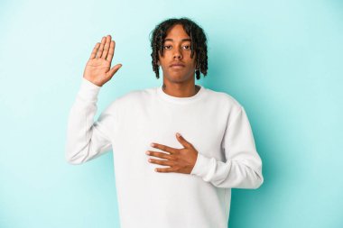 Genç Afrikalı Amerikalı adam mavi arka planda izole edilmiş bir şekilde yemin ediyor, elini göğsüne koyuyor..