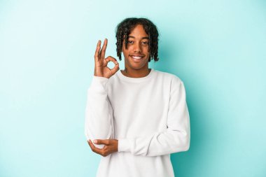 Genç Afrikalı Amerikalı bir adam mavi arka planda izole edilmiş bir şekilde bir göz kırpıyor ve elleriyle iyi bir jest yapıyor..