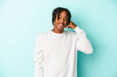 Genç Afrikalı Amerikalı bir adam mavi arka planda izole edilmiş, parmakları olan bir cep telefonu hareketi gösteriyor..