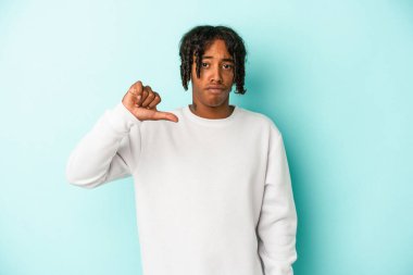 Genç Afro-Amerikan bir adam mavi arka planda izole edilmiş, hoşlanmadığı bir jest gösteriyor, başparmakları aşağıda. Anlaşmazlık konsepti.