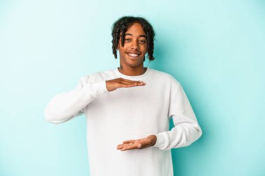 Genç Afro-Amerikalı bir adam mavi arka planda iki eliyle bir şey tutuyor, ürün sunumu..