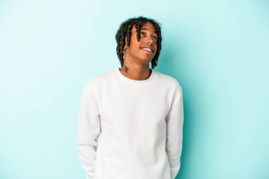 Genç Afrikalı Amerikalı adam mavi arka planda izole edilmiş rahat ve mutlu bir şekilde gülüyor, boynunda dişlerini gösteriyor..