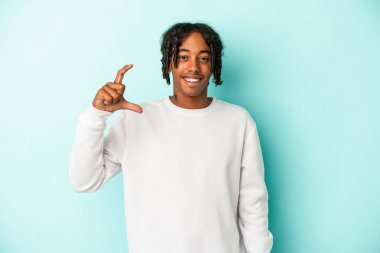 Genç Afrikalı Amerikalı adam mavi arka planda izole edilmiş. Elinde parmakları olan, gülümseyen ve kendinden emin bir şey var..