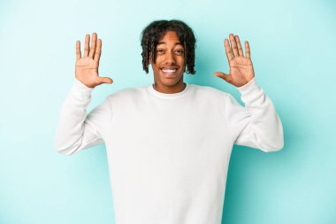Genç Afrikalı Amerikalı bir adam mavi arka planda izole edilmiş. Hoş bir sürpriz, heyecanlı ve el kaldırıyor..