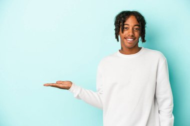 Mavi arka planda izole edilmiş genç Afrikalı Amerikalı bir adam bir avuç içinde fotokopi alanı ve belinde bir el daha gösteriyor..