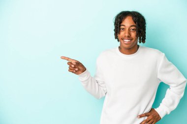 Genç Afrikalı Amerikalı adam mavi arka planda izole edilmiş, mutlu bir şekilde işaret parmağıyla işaret ederek gülümsüyor..