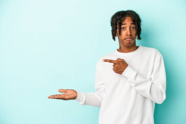 Genç Afro-Amerikan adam mavi arka planda izole edilmiş. Elinde bir fotokopi alanı tutarken heyecanlı..