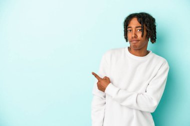 Genç Afrikalı Amerikalı adam mavi arka planda izole edilmiş gülümsüyor ve boş alanda bir şeyler gösteriyor..