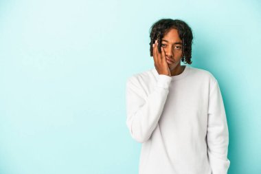 Mavi arka planda izole edilmiş genç Afrikalı Amerikalı üzgün ve dalgın bir şekilde fotokopi odasına bakıyor..