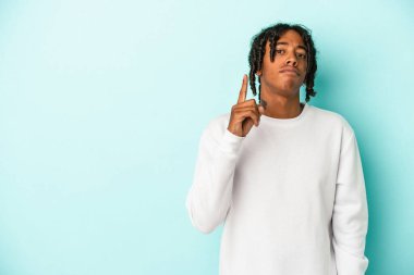 Genç Afrikalı Amerikalı bir adam mavi arka planda izole edilmiş. Bir numarayı parmağıyla gösteriyor..