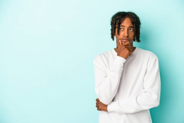 Genç Afrikalı Amerikalı bir adam mavi arka planda izole edilmiş rahat bir şekilde bir şeyin fotokopi odasına baktığını düşünüyor..