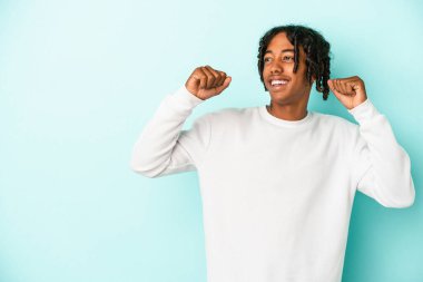 Genç Afrikalı Amerikalı bir adam mavi arka planda izole edilmiş zafer ve galibiyet kavramından sonra yumruğunu kaldırıyor..
