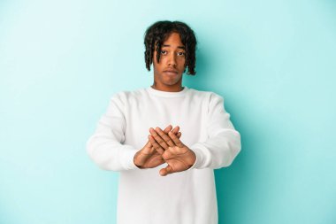 Genç Afrikalı Amerikalı bir adam mavi arka planda izole edilmiş, elini uzatmış, dur işareti göstererek, seni engelliyor..