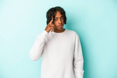 Genç Afrikalı Amerikalı bir adam mavi arka planda izole edilmiş. Parmağıyla tapınağı işaret ediyor. Düşünüyor, bir göreve odaklanıyor..