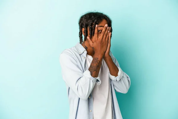 Młody Afroamerykanin Odizolowany Niebieskim Tle Mruga Przez Palce Przestraszony Zdenerwowany — Zdjęcie stockowe