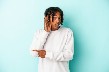 Genç Afrikalı Amerikalı bir adam mavi arka planda izole edilmiş bir şekilde bir dedikoduyu dinlemeye çalışıyor..