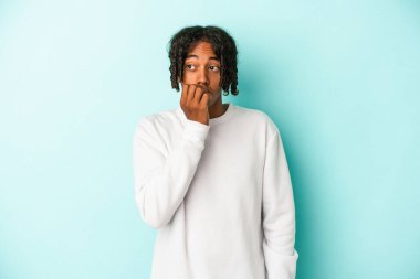 Genç Afrikalı Amerikalı bir adam mavi arka planda izole edilmiş tırnak yiyor, gergin ve çok endişeli..