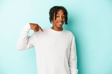 Genç Afrikalı Amerikalı bir adam mavi arka planda izole edilmiş. Elle bir gömlek fotokopi alanını gösteriyor. Gururlu ve kendinden emin.