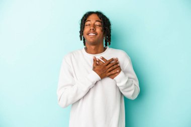Mavi arka planda izole edilmiş genç bir Afro-Amerikan erkeği, avuçlarını göğsüne bastıran dostça bir ifadeye sahiptir. Aşk konsepti.