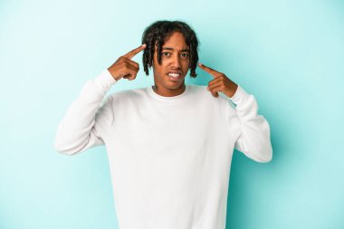 Genç Afro-Amerikalı adam mavi arka planda izole edilmiş işaret parmağıyla hayal kırıklığı jesti gösteriyor..