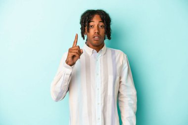 Genç Afro-Amerikalı, mavi arka planda izole edilmiş, ağzı açık, üst tarafı işaret ediyor..
