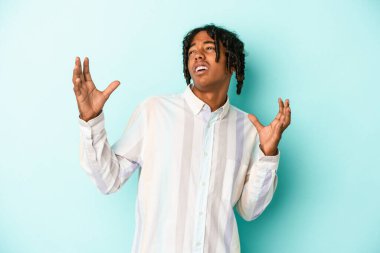 Genç Afrikalı Amerikalı adam mavi arka planda izole edilmiş gökyüzüne haykırıyor, yukarı bakıyor, hayal kırıklığına uğramış..