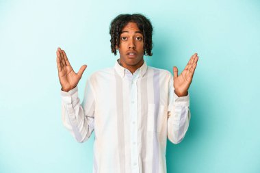 Genç Afrikalı Amerikalı bir adam mavi arka planda izole edilmiş. Şaşırmış ve şok olmuş..