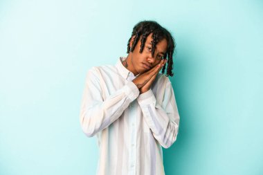 Genç Afrikalı Amerikalı bir adam mavi arka planda izole edilmiş esniyor ve ağzı eliyle kapalı yorgun bir jest yapıyor..