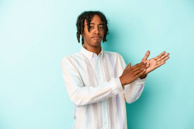 Genç Afrikalı Amerikalı erkek mavi arka planda izole edilmiş enerjik ve rahat hissediyor, kendinden emin ellerini ovuşturuyor..