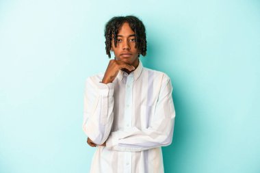 Genç Afrikalı Amerikalı bir adam mavi arka planda izole edilmiş şüpheli, belirsiz, seni inceliyor..