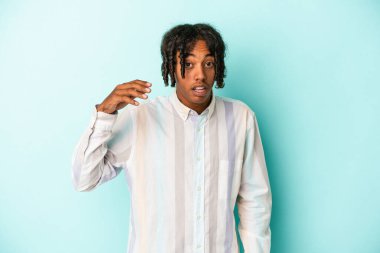 Genç Afrikalı Amerikalı bir adam mavi arka planda izole edilmiş bir şekilde bir şeylere gülüyor, elleriyle ağzını kapatıyor..