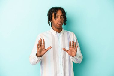 Genç Afrikalı Amerikalı bir adam mavi arka planda izole edilmiş, tiksinti belirtisi gösteren birini reddediyor..