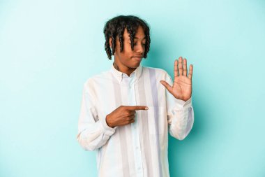 Genç Afro-Amerikalı adam mavi arka planda izole edilmiş. Gülümsüyor. Beş numarayı parmaklarıyla gösteriyor..