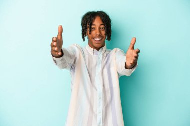 Mavi arka planda izole edilmiş genç Afrikalı Amerikalı adam kameraya sarıldığı için kendinden emin hissediyor..