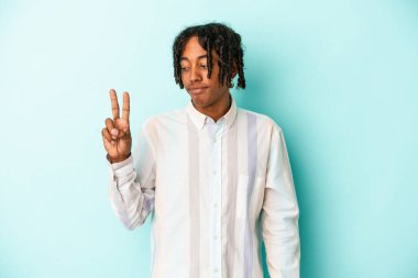 Genç Afrikalı Amerikalı adam mavi arka planda izole edilmiş neşeli ve kaygısız parmakları olan bir barış sembolü gösteriyor..
