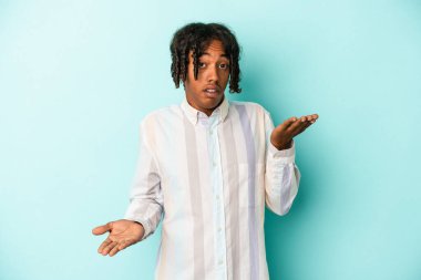 Mavi arka planda izole edilmiş genç Afrikalı Amerikalı adam kollarıyla ölçek oluşturuyor, mutlu ve kendinden emin hissediyor..