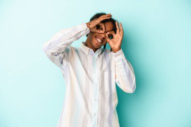 Genç Afro-Amerikalı adam mavi arka planda izole edilmiş, gözlerinde sorun yok işareti var.