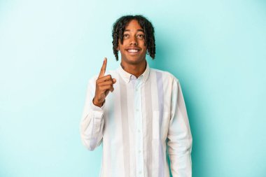 Mavi arka planda izole edilmiş genç Afrikalı Amerikalı iki parmağı da boş bir alan gösteriyor..