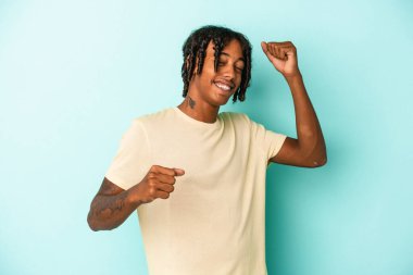 Genç Afrikalı Amerikalı adam mavi arka planda izole edilmiş özel bir günü kutluyor, atlıyor ve enerjiyle kollarını kaldırıyor..