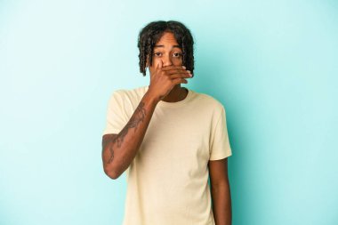 Genç Afro-Amerikalı adam mavi arka planda izole edilmiş ağzı kapalı ve elleri endişeli görünüyor..