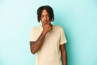 Genç Afro-Amerikalı bir adam mavi arka planda izole edilmiş bir şekilde bir strateji planlıyor, bir işin nasıl olacağını düşünüyor..