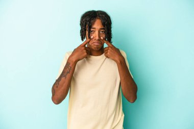 Genç Afrikalı Amerikalı bir adam mavi arka planda izole edilmiş ağlıyordu, bir şeyden mutsuzdu, acı ve kafa karışıklığı konsepti vardı..