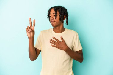 Genç Afrikalı Amerikalı adam mavi arka planda izole edilmiş bir şekilde yemin ediyor, elini göğsüne koyuyor..