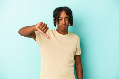 Genç Afro-Amerikalı adam mavi arka planda izole edilmiş baş parmağını aşağı gösteriyor ve hoşlanmadığını ifade ediyor..