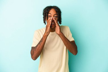 Genç Afrikalı Amerikalı bir adam mavi arka planda izole edilmiş. Dedikodu yapıyor, bir şeyleri bildiriyor..