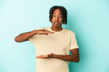 Genç Afro-Amerikalı bir adam mavi arka planda iki eliyle bir şey tutuyor, ürün sunumu..